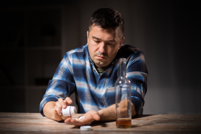 Depression, drug abuse and addiction people concept - unhappy drunk man with bottle of alcohol and pills committing suicide by overdosing on medication at night